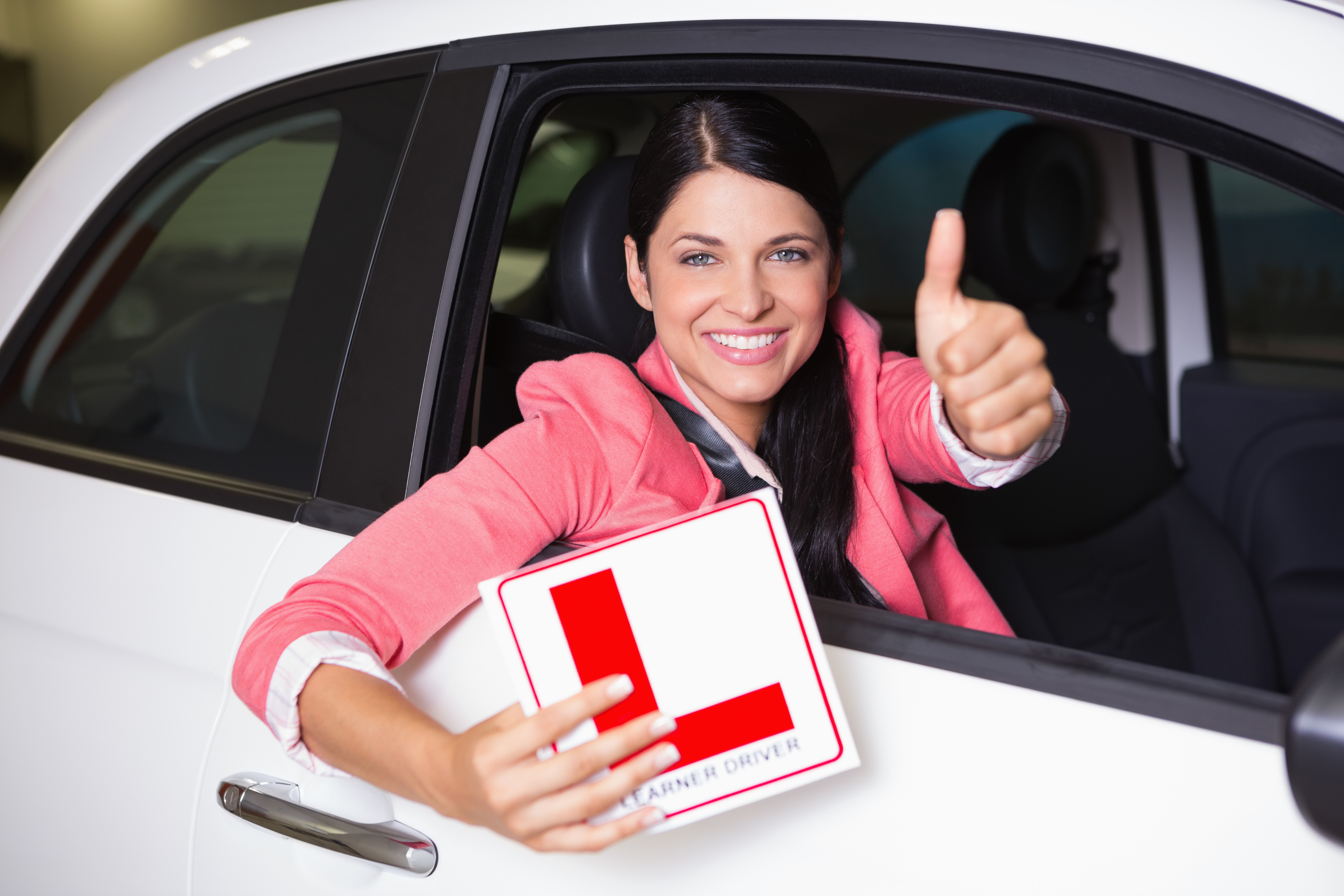 Woman gesturing thumbs up holding a learner driver sign at new car showroom