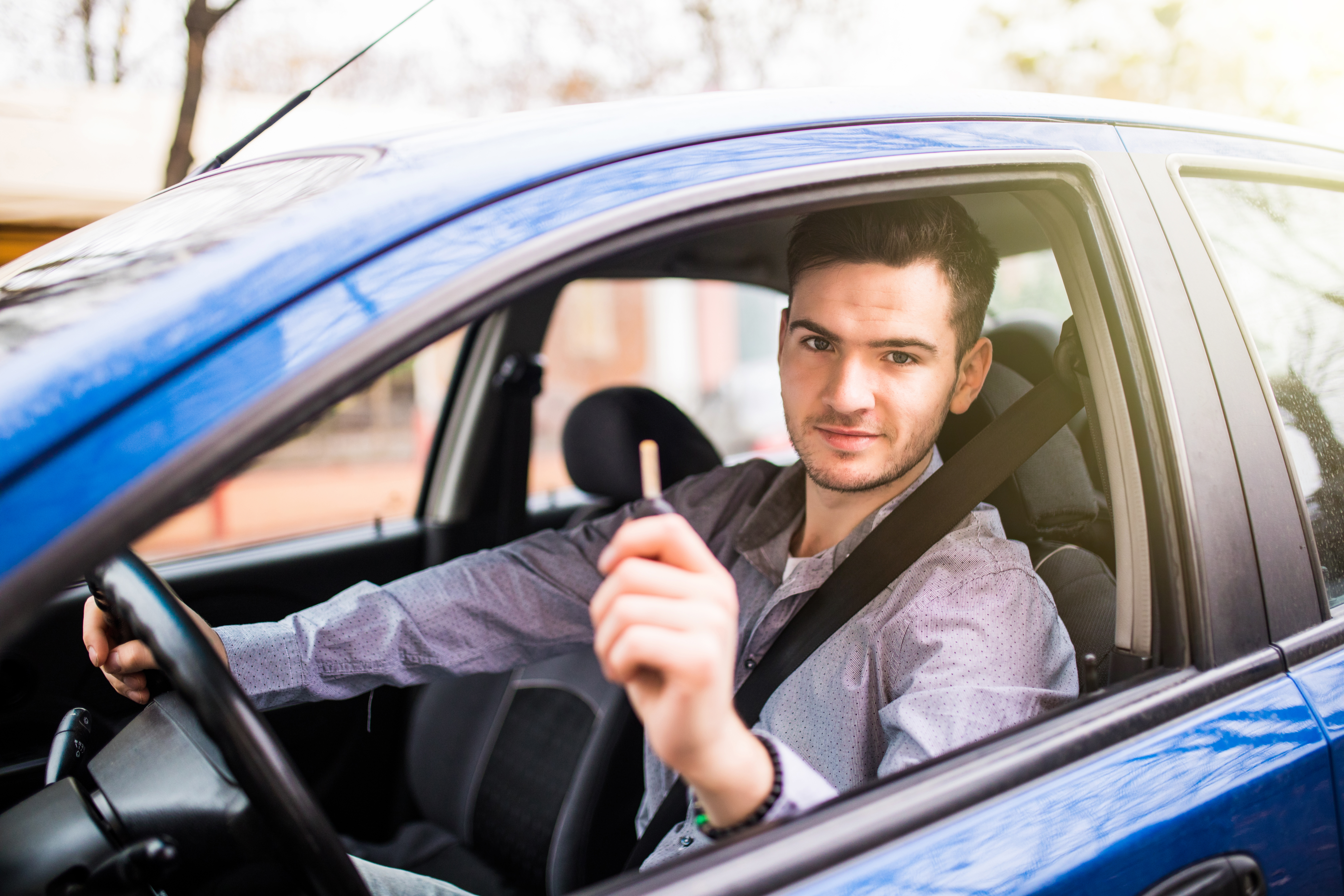 Young handsome man driving his new car, holding out keys
